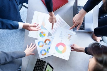 Grupo de personas analizando gráficos y reportes impresos sobre una mesa de trabajo.